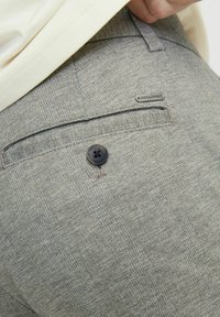 Pantaloni grigi su misura con un motivo a quadri sottile, dotati di un bottone nero e un'etichetta in metallo sul retro. Tessuto dalla texture liscia.