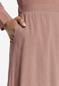 Rosa kjol med en mjuk, flödande textur, en sidoficka och en figursydd midja, uppvisad med en hand i fickan.