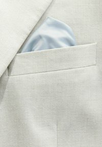 Poche de veste de costume beige clair avec un mouchoir de poche en satin bleu pâle soigneusement plié inséré.