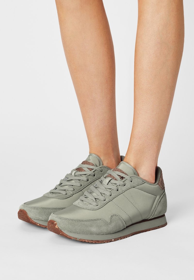 Hellgrüne Sportschuhe aus einer Kombination von Wildleder und glattem Material, mit Schnürdesign und strukturierten braunen Akzenten an der Ferse.