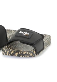 Črne drsne sandale z teksturirano naramnico in logotipom, ki imajo podplat s patternom v odtenkih bež in rjave.