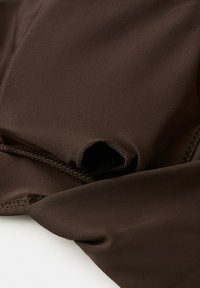 Primo piano di tessuto marrone liscio con cucitura ordinata e una piccola sezione piegata su uno sfondo bianco.