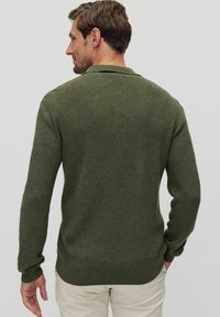 Mörkgrön stickad tröja med ribbat mönster, långa ärmar och en något figursydd form. Inga synliga mönster eller logotyper.