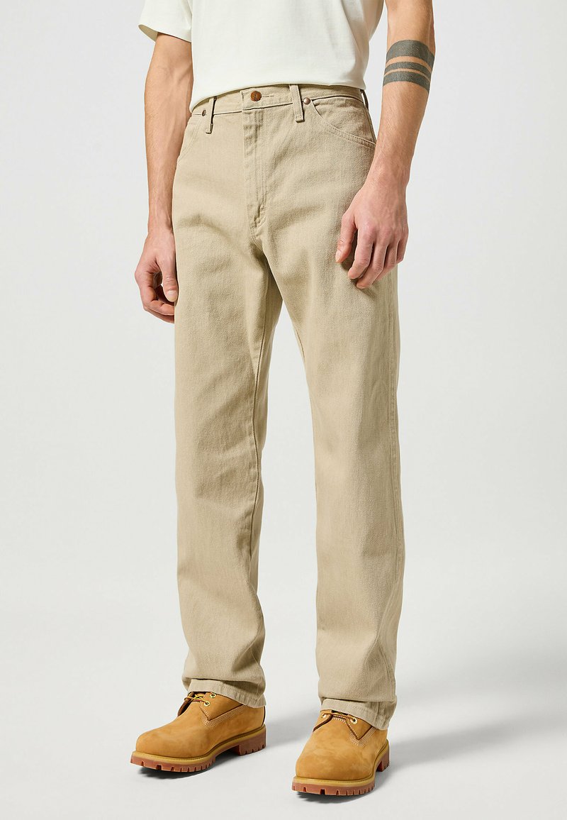 Beige cotton trousers with a straight-leg design, featuring front pockets and a brown button. Worn with light brown lace-up boots.