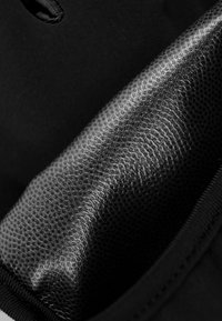 Schwarzes, strukturiertes Material mit einem glatten Glanz, teilweise aufgerollt. Präsentiert dezente Muster und eine kontrastierende matte Kante entlang der Naht.