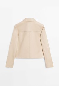 Beige cropped jakke med lange ærmer, lige krave og synlige sømdetaljer på en hvid baggrund.