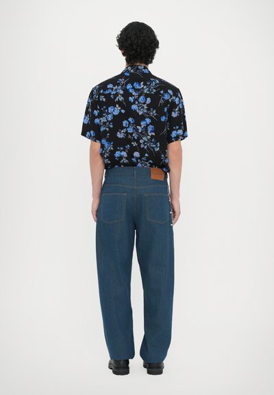 Kortärmad svart skjorta med blå blommönster, kombinerad med blå denimbyxor som har en brun läderetikett och två bakfickor.