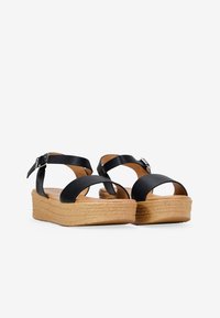 Black leather wedge sandals with adjustable ankle strap, textured upper, and light-colored, grooved cork platform.