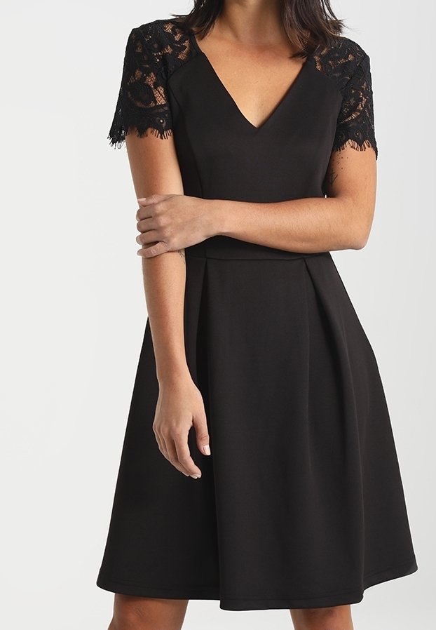 Abito nero con scollo a V e maniche corte in pizzo. La gonna si allarga dalla vita, caratterizzata da una texture liscia e un design semplice.
