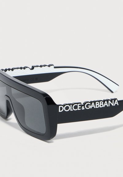 Μαύρα ορθογώνια γυαλιά ηλίου με σκουρόχρωμους φακούς και έντονο λευκό λογότυπο «Dolce & Gabbana» σε παχιά πλευρικά μπράτσα.
