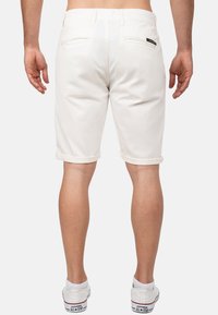 Shorts en denim blanc avec des revers, deux poches arrière et une branding subtile à la taille. Portés avec des baskets blanches.
