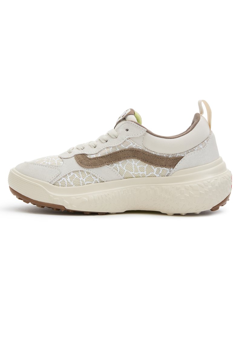 Sneaker crema e beige con suola texturizzata, dettagli in suede, tomaia in mesh decorato e linguetta sul tallone, mostrata in profilo laterale.
