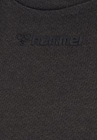 Gros plan sur un tissu gris foncé texturé avec un logo noir en relief « hummel » et un emblème de bourdon sur l'encolure du vêtement.