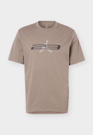 T-shirt beige à manches courtes avec un logo stylisé de joueur de basket-ball en noir et blanc, centré au-dessus de deux bandes horizontales noires.