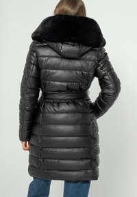 Zwarte gewatteerde jas met een nepbontkraag, een ceintuur in de taille en verticale stiksels. Het ontwerp benadrukt warmte en een slanke silhoeët.