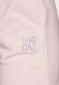 Bladoróżowy materiał z teksturowanej tkaniny. Wytłoczone logo w białym kolorze po lewej stronie. Widoczne detalowanie szwów wzdłuż krawędzi.