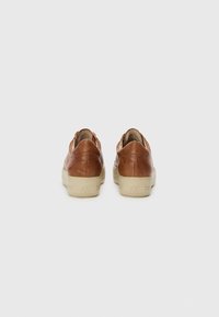 Baskets en cuir marron avec un profil bas, semelle en caoutchouc crème et accents cousus. Texture lisse et design minimaliste.