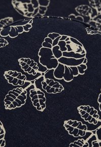 Blomstertekstil med en mørk marineblå bakgrunn og hvite roser og bladmønstre. Materialet ser ut til å være vevd med en myk tekstur.