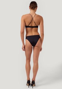 Svart bikini med ett korsande ryggdesign, matchande högmidjade underdelar och en slät textur. Bärs med svarta högklackade skor.