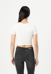 Balts ribots  crop top krekls, pieguļošs dizains, apvienots ar tumši pelēkiem džinsiem, kuru jostā un aizmugurējās kabatās ir zelta "ONLY" logo.