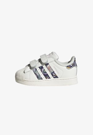 Basket blanche pour tout-petit avec deux bandes Velcro, bandes Adidas à motifs et languette de talon à motifs sur une semelle blanche.