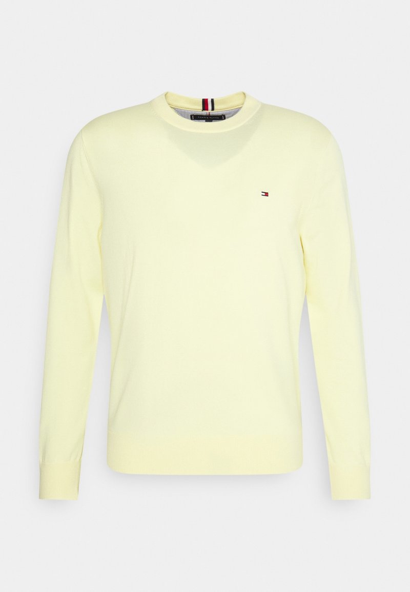 Pull à col rond à manches longues de couleur jaune clair avec petit logo rouge, blanc et bleu sur la poitrine et détail rayé à l'intérieur du col.