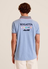 Lichtblauw poloshirt met geborduurd "REGATTA" en kleurrijke accenten op de achterkant. Heeft een gemêleerde kraag en korte mouwen.