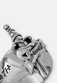 Srebrni prsten s detaljnim dizajnom koji sadrži mač i vrpcu s natpisom "BEFORE." Glatka površina s poliranim teksturom.