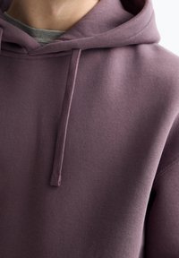 Felpa viola realizzata in tessuto morbido, con cappuccio regolabile e una superficie semplice e strutturata. Nessun logo o motivo visibile.