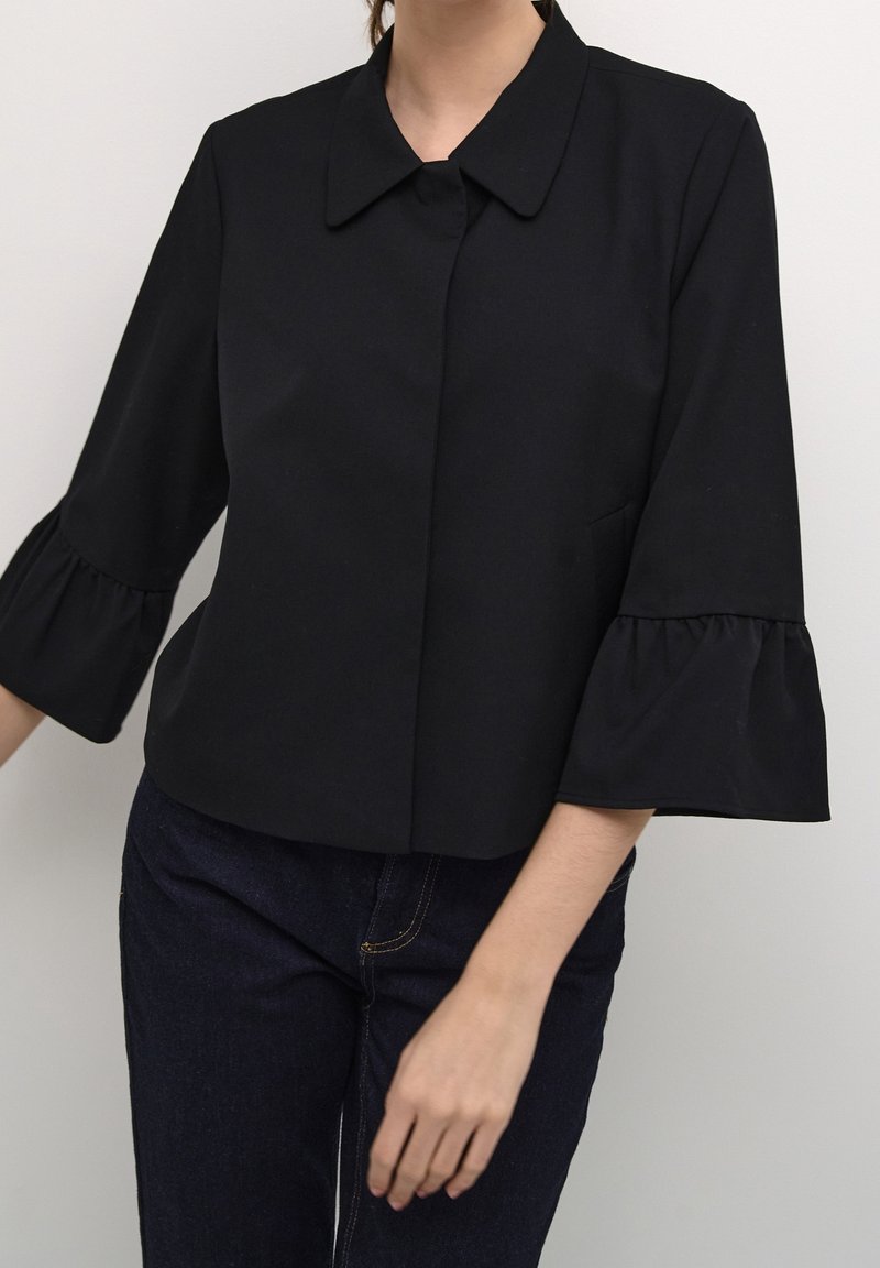 Svart beskuren skjorta med krage, trekvartslånga ärmar med volangdetaljer, och mjukt tyg. Enkelt mönster, minimal detaljering.