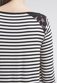 Svart och vit randig långärmad topp med spetsdetalj på axeln. Har en mjuk textur och en rundad halsringning.