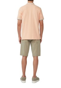 Jasno brzoskwiniowa koszulka polo z kontrastowym jasnoniebieskim wykończeniem, połączona z beżowymi szortami dżinsowymi i szarymi trampkami. Prosty design, wygodny krój.