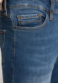 Középkék farmernadrág látható varrással. Klasszikus dizájn, elülső és hátsó zsebekkel, valamint enyhén kopott hatással.