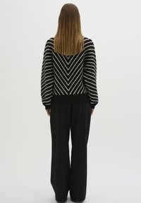 Maglione a strisce nere e bianche con un motivo a zigzag, maniche lunghe e polsini a coste, abbinato a pantaloni neri a gamba larga.