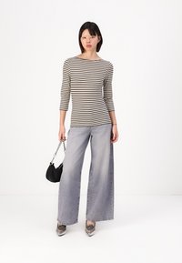 Rutet langermet topp i svart og krem, kombinert med vide lysegrå jeans. Modellen holder en svart veske og har på seg grå mønstrede sko.
