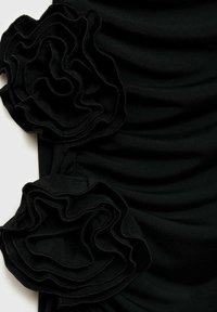 Tissu noir à texture froncée, présentant deux appliqués floraux superposés à gauche. Les volants ajoutent de la profondeur au design.