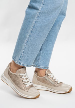 Beige Turnschuhe mit metallischen Akzenten, weißen Schnürsenkeln, einer strukturierten Oberseite und einer Gummisohle. Kombiniert mit hellblauen, gekürzten Jeans.