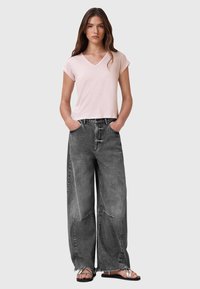 T-shirt V-neck rosa chiaro, maniche corte, abbinato a jeans neri di denim a gamba larga e alta vita, con orli sfilacciati e dettagli di cucitura a vista.