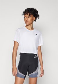Hvit kortermet t-skjorte med svart logo, kombinert med svarte shorts med grå paneler og hvite detaljer. Jevnt stoff, atletisk passform.