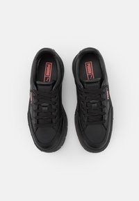 Schwarze Sportschuhe mit einem glatten Lederoberteil, robuster Gummisohle, runder Zehenform und schwarzen Schnürsenkeln, verziert mit pinken Puma-Logo-Akzenten.