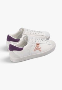 Zapatillas de cuero blancas con detalles de ante morado, que presentan un bordado de calavera y huesos cruzados en rosa en el costado y suelas de goma texturizadas.