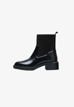Svart ankelboot med en slät, polerad läderfinish. Har ribbade elastiska sidopanels och en blockklack med en gyllene accent.