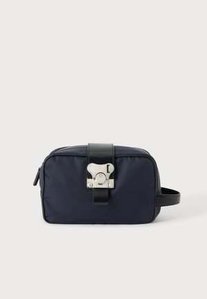 Kompakte dunkelblaue Kulturtasche mit schwarzem Lederband und silberner Metallschnalle vorne sowie einem seitlichen Griff.