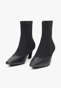 Czarne botki za kostkę zamszową cholewką, spiczastym noskiem i błyszczącą skórzaną nasadką noska. Niski blokowy obcas i bezszwowy design.