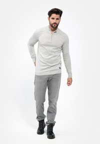 Pullover grigio chiaro a maniche lunghe con collo a zip, realizzato in tessuto testurizzato, abbinato a pantaloni grigi e stivali neri con lacci. Dettaglio logo discreto sul pullover.