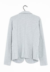 Harmaa bleiseri, pitkät hihat, kevyt kangas, räätälöity malli, kaareva helma ja sivutaskut. Kauluksen yksityiskohta näkyy pääntien kohdalla.