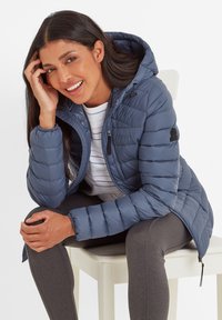 Blue padded jacket with a hood, zippered front, elastic cuffs, and logo details. Worn over a striped shirt and grey leggings.