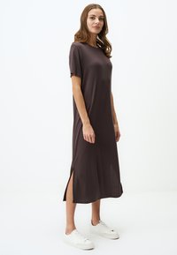 Robe marron à mi-mollet avec des manches courtes, fentes latérales et coupe décontractée, accompagnée de baskets blanches sur un fond neutre.