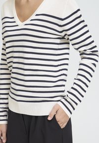 Pull rayé à col en V, présentant des rayures horizontales bleu marine et crème, des poignets côtelés et une texture en maille douce et légère.