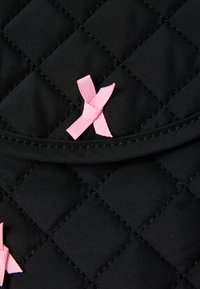 Stoffă quilted de culoare neagră cu un capac pliabil decorat cu panglici roz. Suprafața este netedă, cu modele de diamant create prin cusătură.